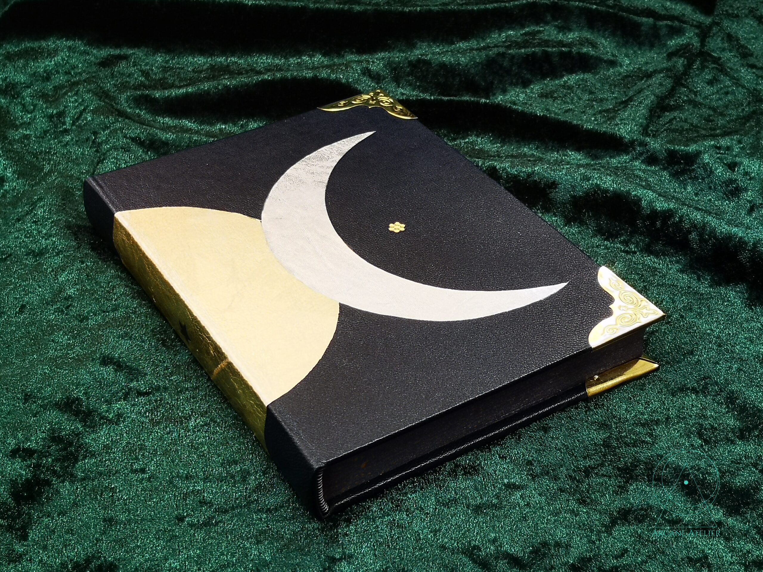 Three-quarter view of a black leather journal showing part of the triple moon motif with the crescent and half of the full moon.